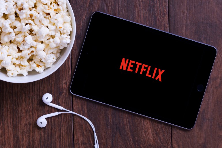 New York, USA - October 12, 2018: Table with popcorn bottle and Netflix logo on Apple Ipad mini and earphone. Netflix is a global provider of streaming movies and TV series.