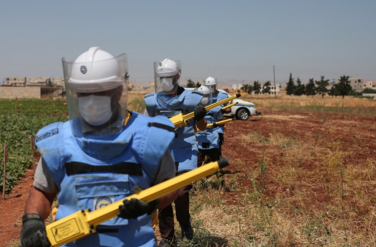 Members of the Syrian civil defence known as the White Helmets, equipped with protective outfits, get ready to search and neutralise unexploded weapons in a field, on the outskirts of al-Jinah village in Syria's northern Aleppo province, on June 23, 2022. The shelling and airstrikes responsible for a large part of the Syrian war's half million deaths have decreased in recent years. But explosive remnants laid by all sides in the 11-year-old conflict are causing more deaths in Syria than anywhere else in the world, according to the United Nations. (Photo by Aaref WATAD / AFP)