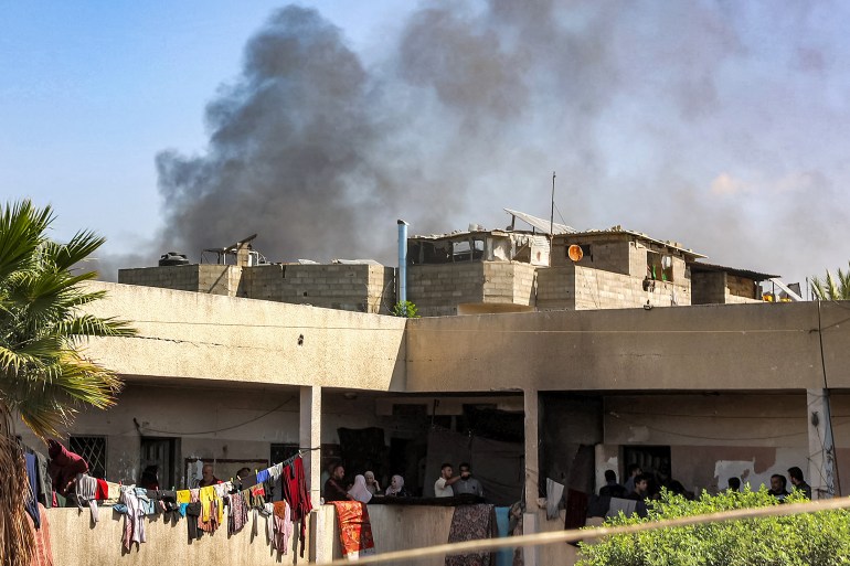 Smoke plumes billow behind as people gather in the balcony corridors of the Rafei school serving as a displacement shelter in the Jabalia camp for Palestinian refugees in the northern Gaza Strip on October 9, 2024 amid the ongoing war in the Palestinian territory between Israel and Hamas. (Photo by Omar AL-QATTAA / AFP)