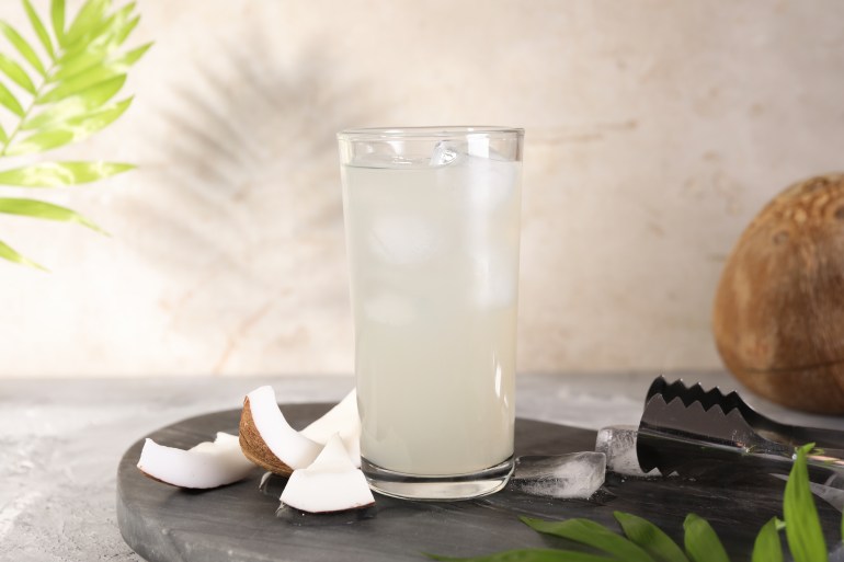 Glass of coconut water, ice cubes and nuts on grey table