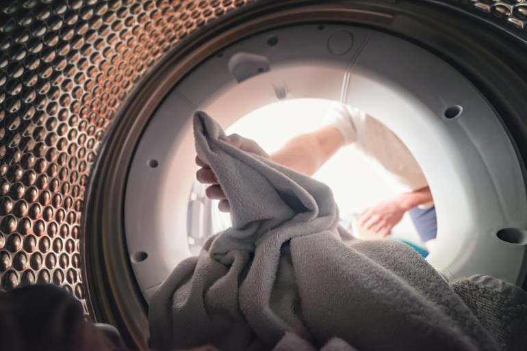 View from inside the drum of a washing machine: a man loads or unloads laundry. Laundry. Interior view of the washing machine.