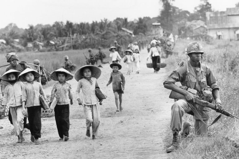 Vietnam War U.S. Vietnamese Civilians In an area heavily infiltrated by Viet Cong, a U.S. 1st Division soldier guards Route 7 as Vietnamese market women and schoolchildren return home to the village of Xuan Dien from Ben Cat, December 1965. (AP Photo/Horst Faas)