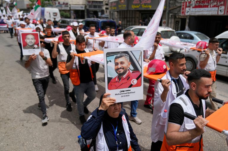 A paramedic holds posters with names and pictures of fellow relief workers who lost their lives in the line of humanitarian duty, during a symbolic funeral for 48 fallen Palestinian Red Crescent Society members during the Israel Hamas war in Gaza, according to a PRCS statement, marking the World Day of Red Cross and Red Crescent, in the West Bank city of Ramallah Monday, May 12, 2025. (AP Photo/Nasser Nasser)