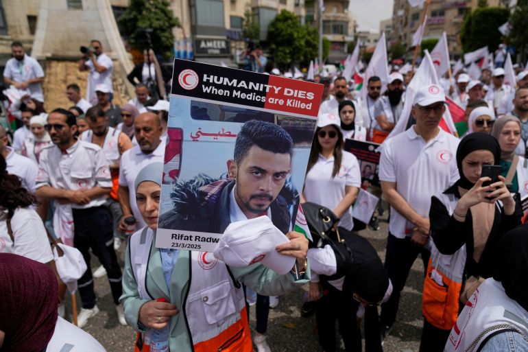 Paramedic hold posters with names and pictures of fellow relief workers who lost their lives in the line of humanitarian duty, during a symbolic funeral for 48 fallen Palestinian Red Crescent Society members during the Israel Hamas war in Gaza, according to a PRCS statement, marking the World Day of Red Cross and Red Crescent, in the West Bank city of Ramallah Monday, May 12, 2025. (AP Photo/Nasser Nasser)