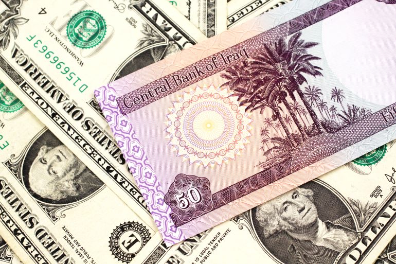 A purple Iraqi fifty dinar bank note close up in macro with an assortment of American one dollar bills