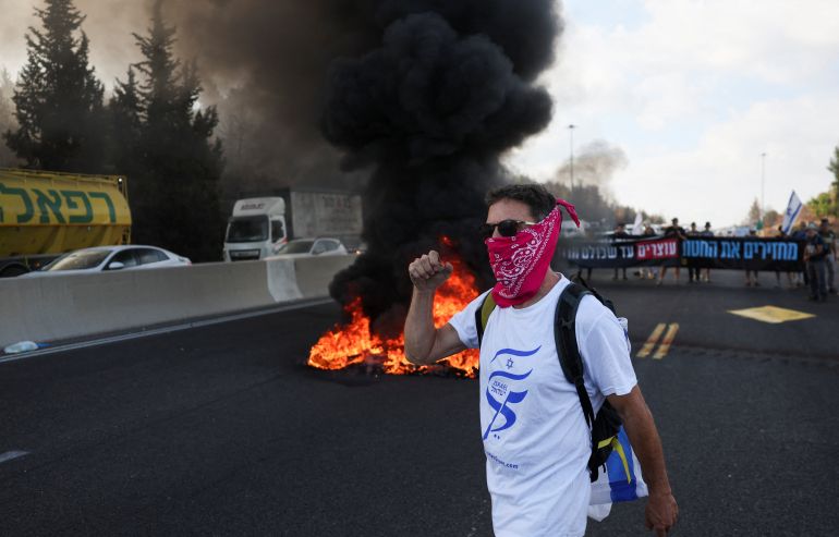 A man gestures in front of burning tyres as people block Israel's main highway connecting Jerusalem and Tel Aviv near Latrun after families of hostages have called for a nationwide strike to demand the return of all hostages and an end to the war in Gaza, Latrun Israel August 17,2025 REUTERS/Ronen Zvulun